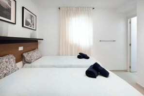 Une chambre d’hôtel avec deux lits, une tête de lit en bois, des coussins à motifs, une fenêtre avec des rideaux légers et une porte.