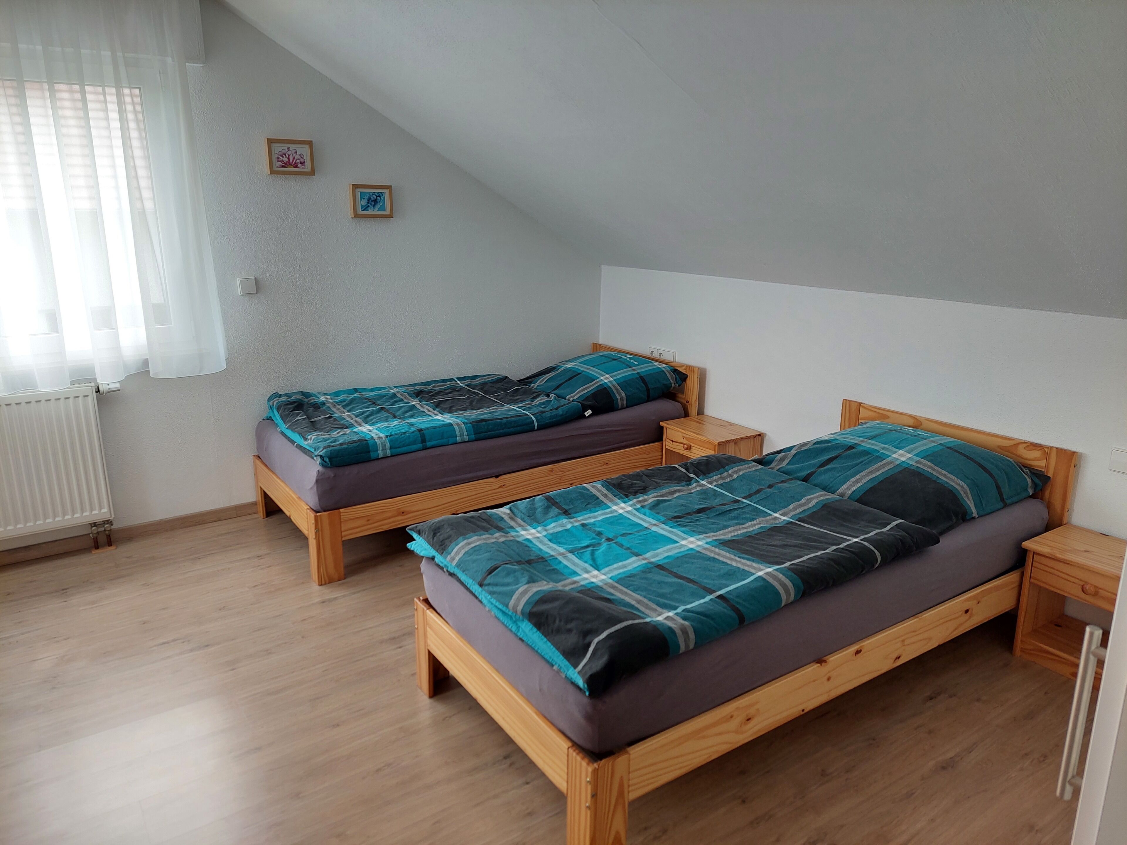 Une chambre à coucher avec deux lits en bois, un radiateur blanc et une fenêtre ornée de rideaux légers.