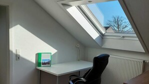 Un pequeño dormitorio en el ático con tragaluces, un escritorio, una silla y un radiador.