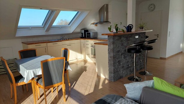 Una cocina moderna con tragaluces, un comedor con mesa y sillas, y una barra con un taburete.