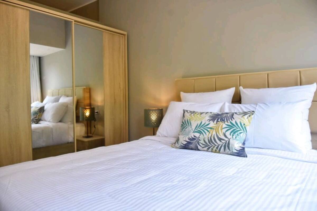 Una habitación de hotel con una cama, un espejo, una mesita de noche con una lámpara y un armario.