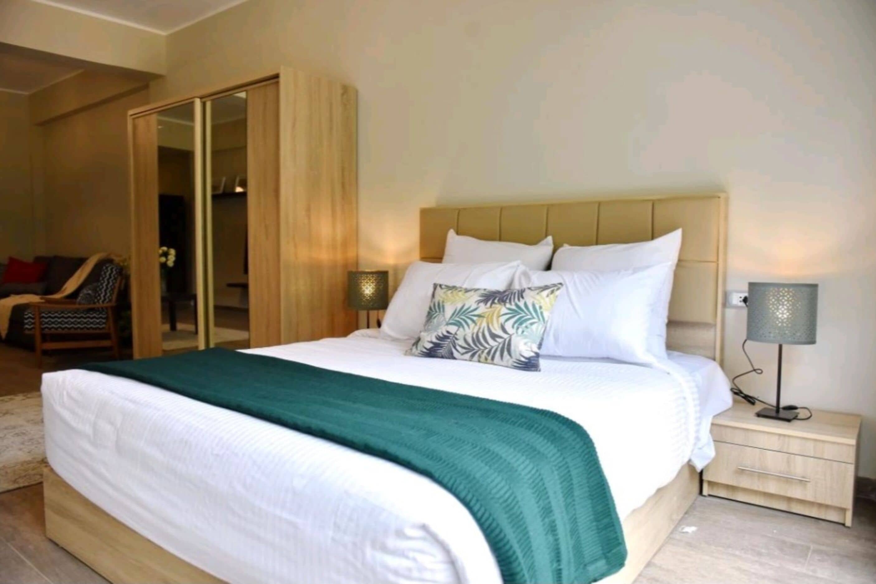 A bedroom with a large bed, a nightstand, a lamp, a chair, and a wardrobe.