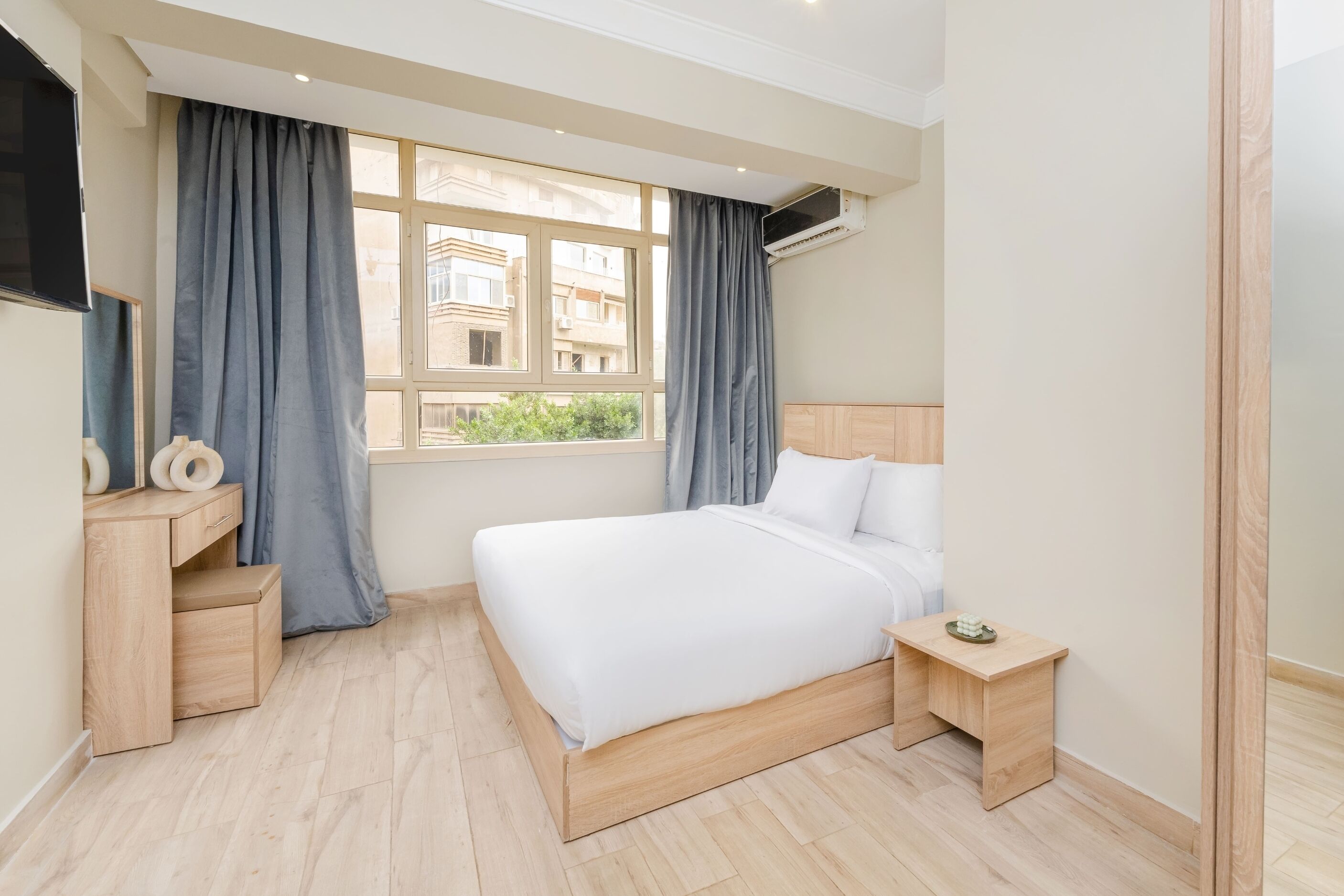 A bedroom with a bed, bedside tables, a TV, and a window with curtains.