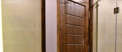 A bathroom with a wooden door, a glass shower enclosure, and a sink with a plant.