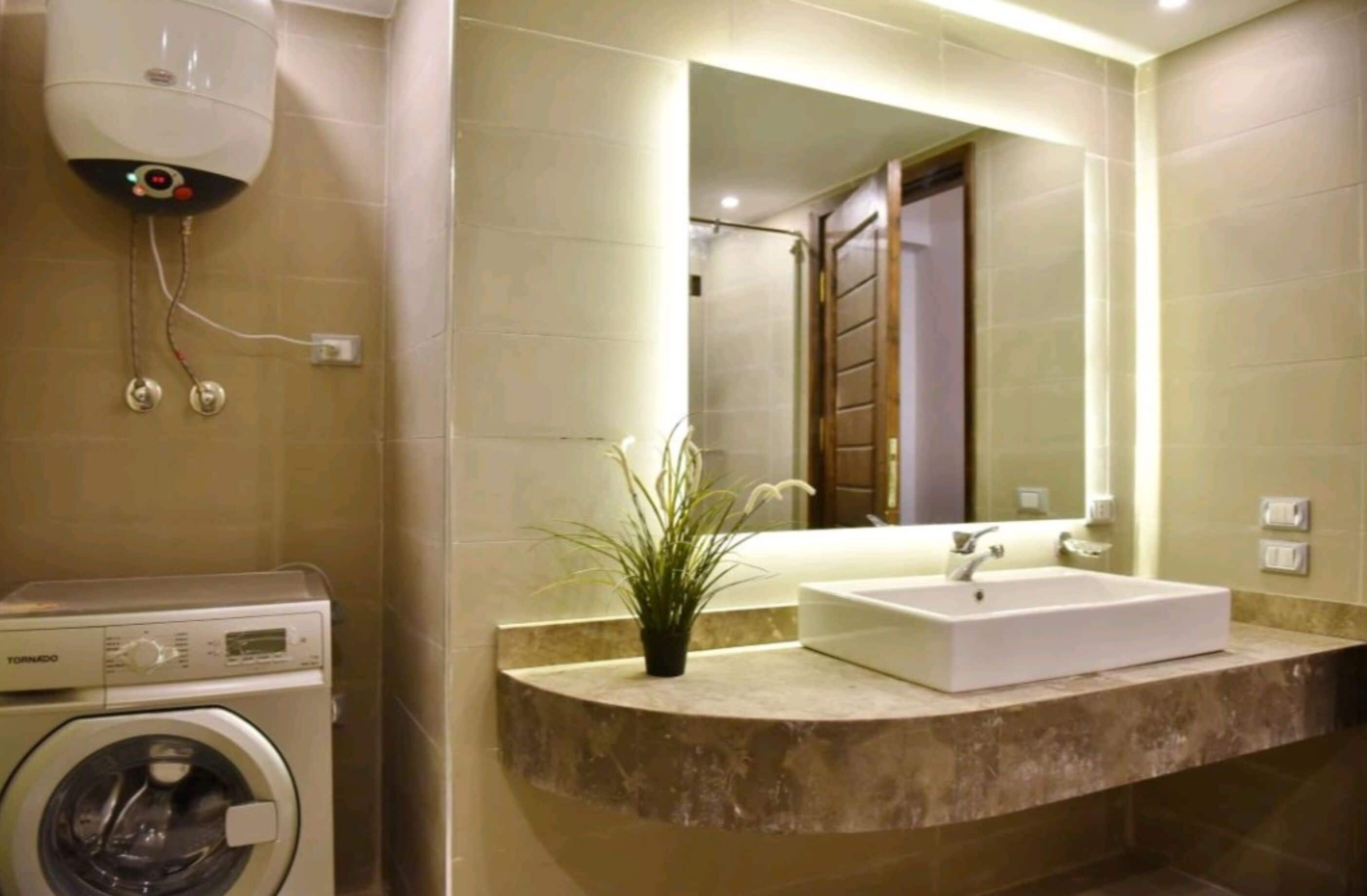 A modern bathroom with a built-in washing machine, a sink with a mirror, and a potted plant.