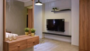 Een moderne kamer met een grote spiegel, een houten wastafelmeubel, potplanten, een wandgemonteerde televisie en een hanglamp.
