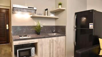 Une cuisine compacte équipée d’un four à micro-ondes encastré, d’un réfrigérateur noir, d’un évier et d’un petit plan de travail agrémenté d’une plante en pot.