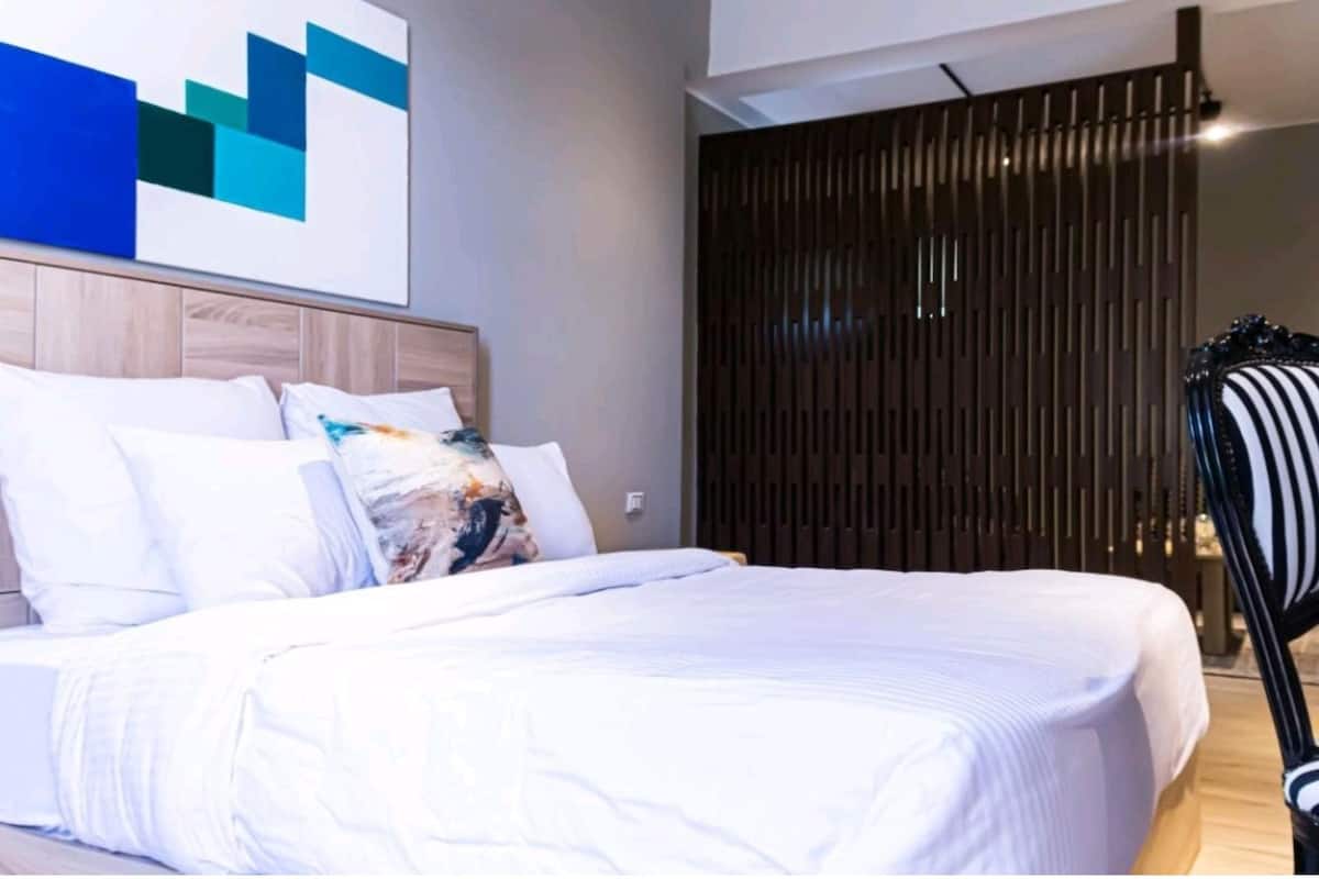 Un dormitorio con cama, cabecera, pared con pintura geométrica y separador de madera con listones.