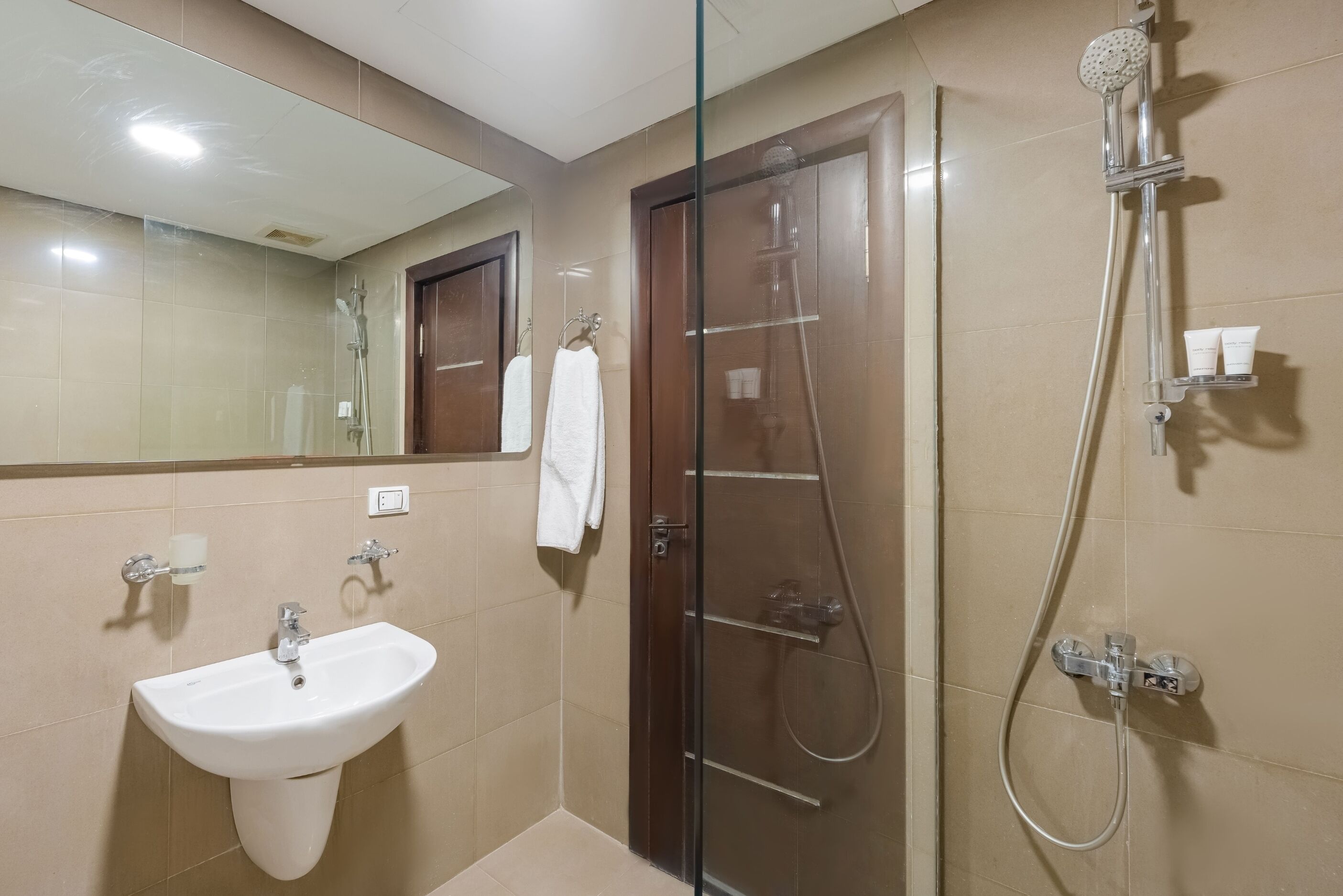 Baño con lavabo, espejo, cabina de ducha de vidrio y toallero.