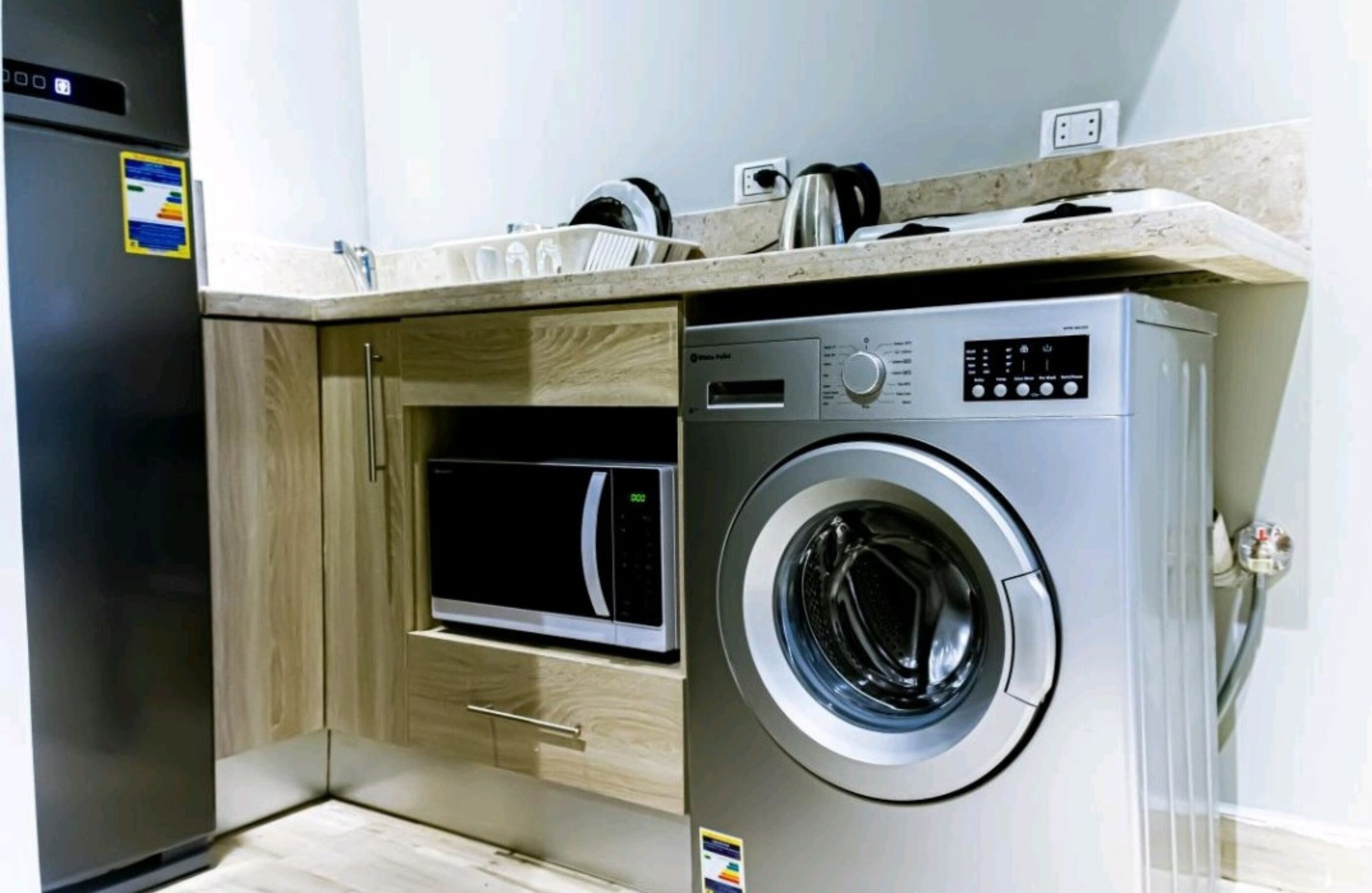A compact kitchen with a built-in microwave, a washing machine, and a wooden cabinet.