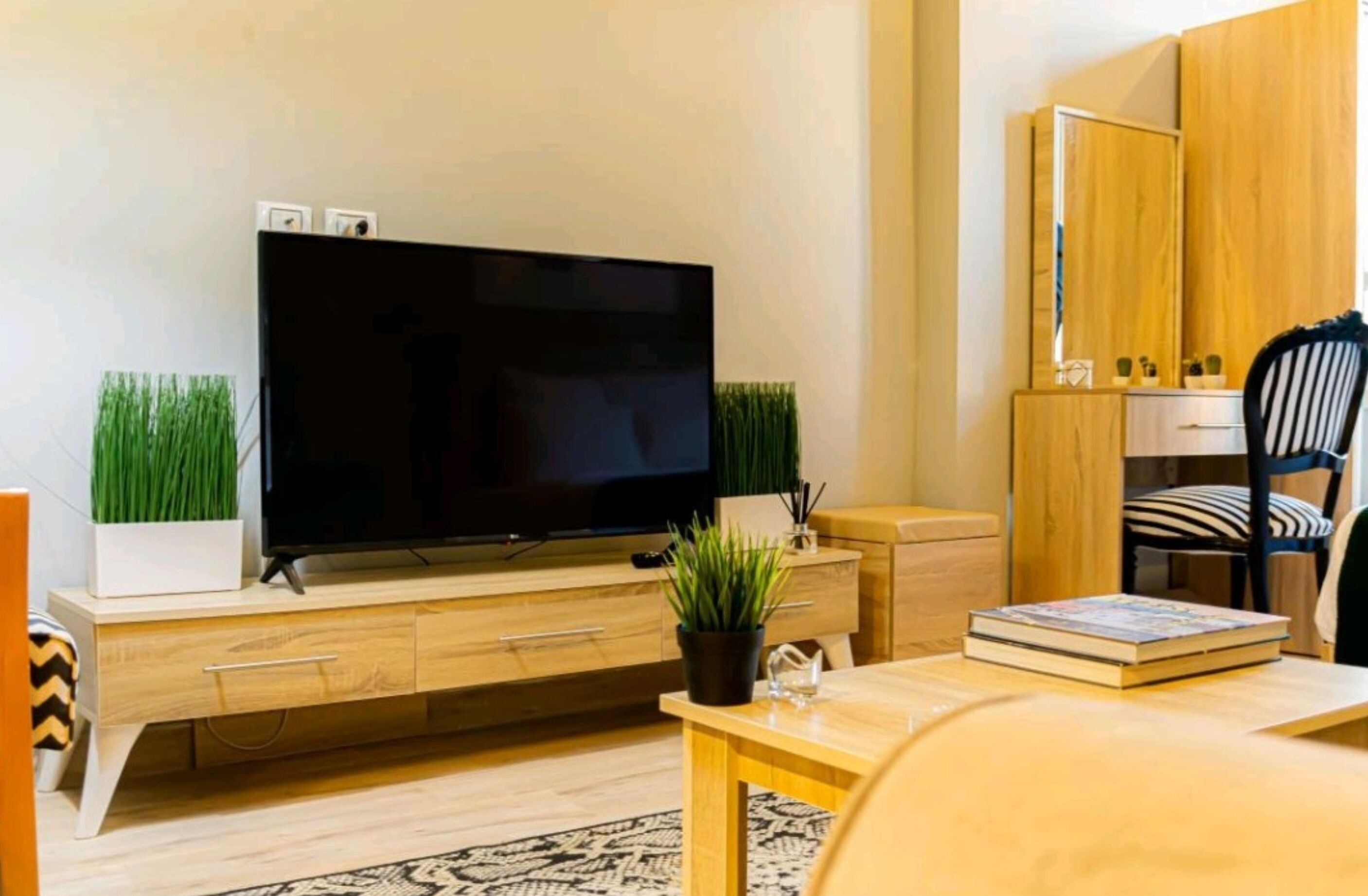 Una sala de estar moderna con un televisor de pantalla plana, muebles de madera, una mesita con un libro y una planta en maceta.