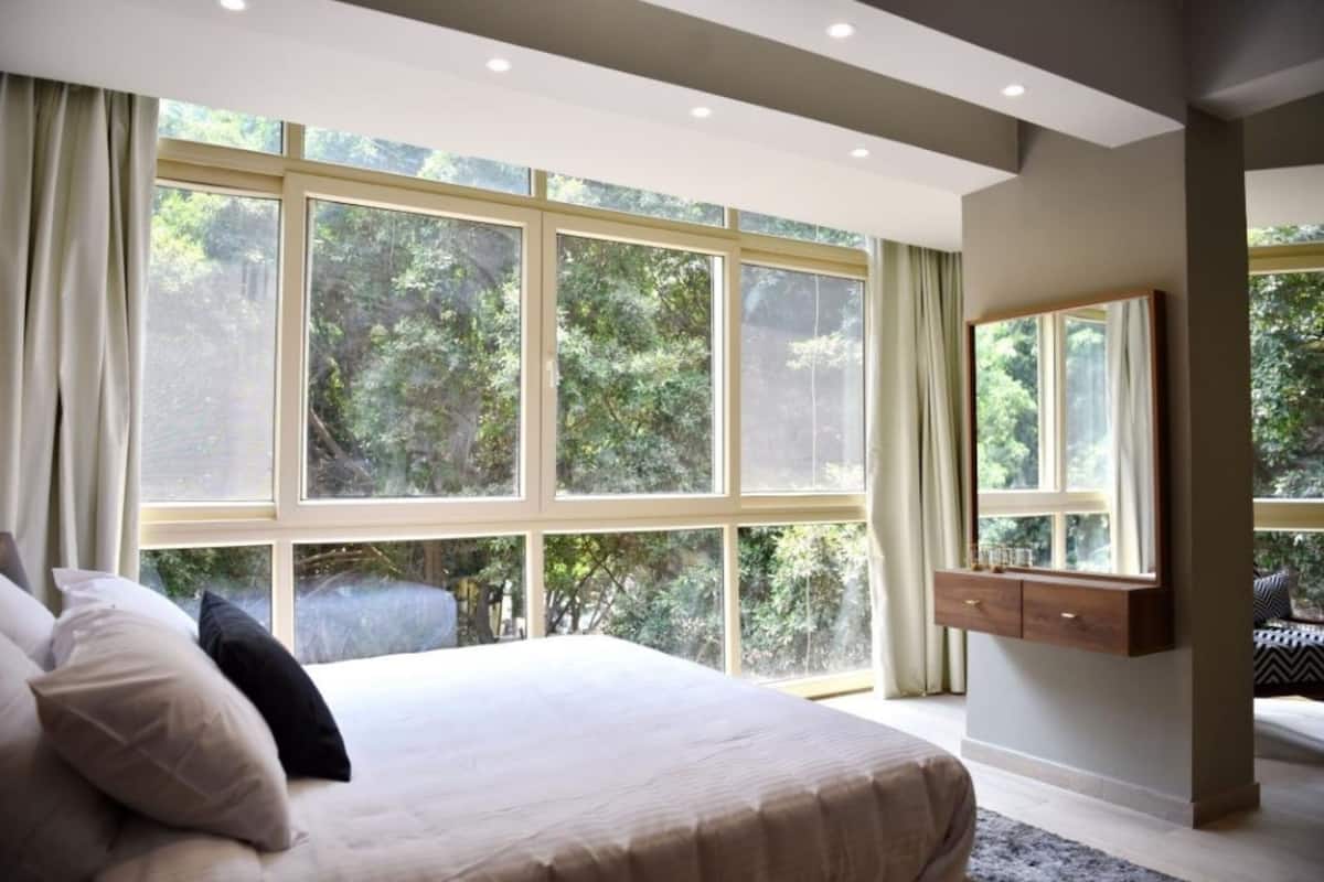 Un dormitorio con una ventana grande, una cama, una mesita de noche y un espejo.