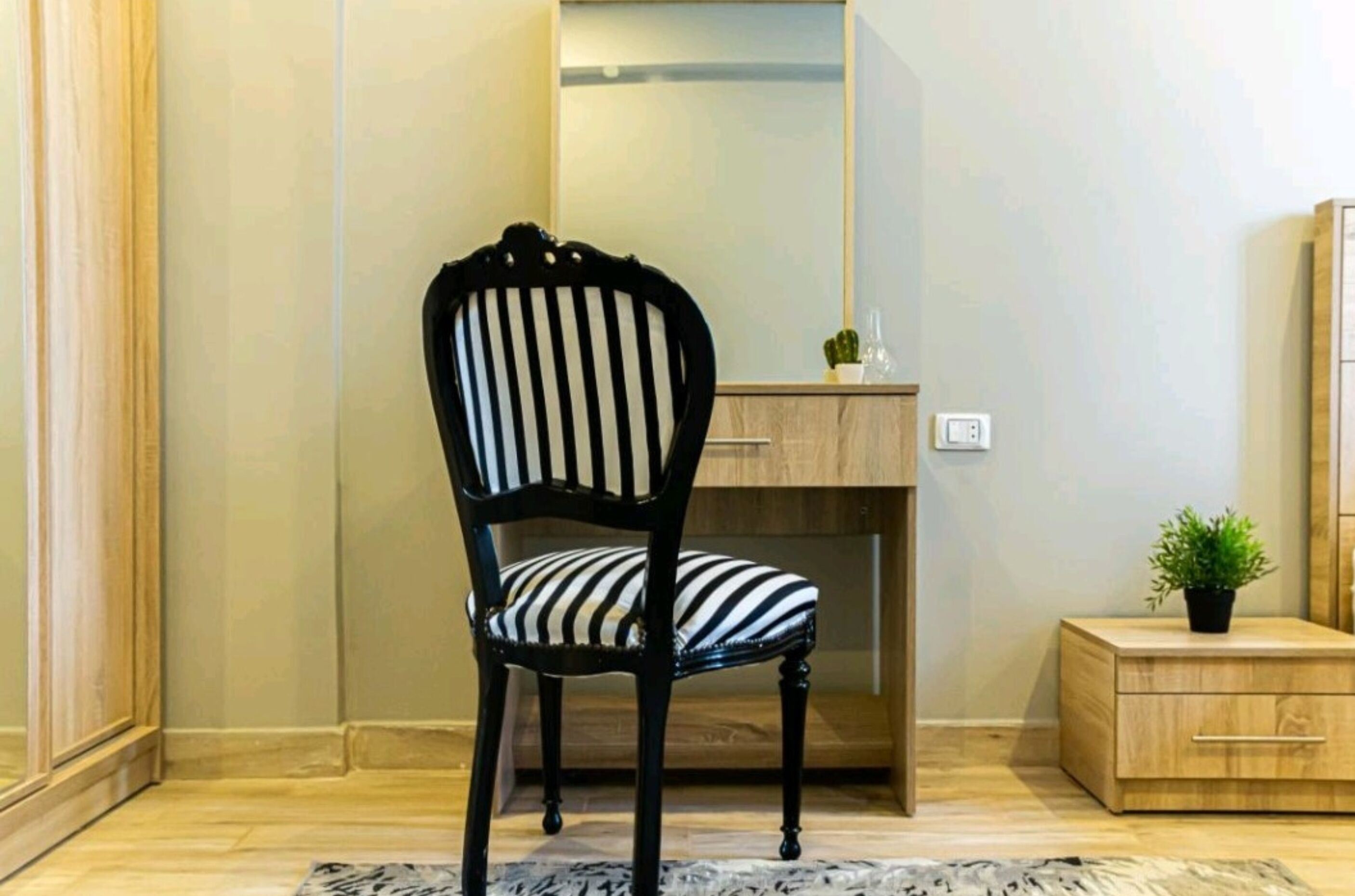 Una silla con un cojín a rayas, un escritorio de madera, una pequeña cómoda y una planta en maceta.