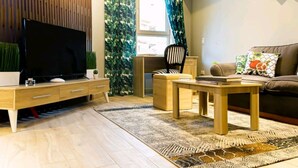 Een moderne woonkamer met een flatscreen televisie, houten meubels, een gekleurd vloerkleed en een bank met decoratieve kussens.