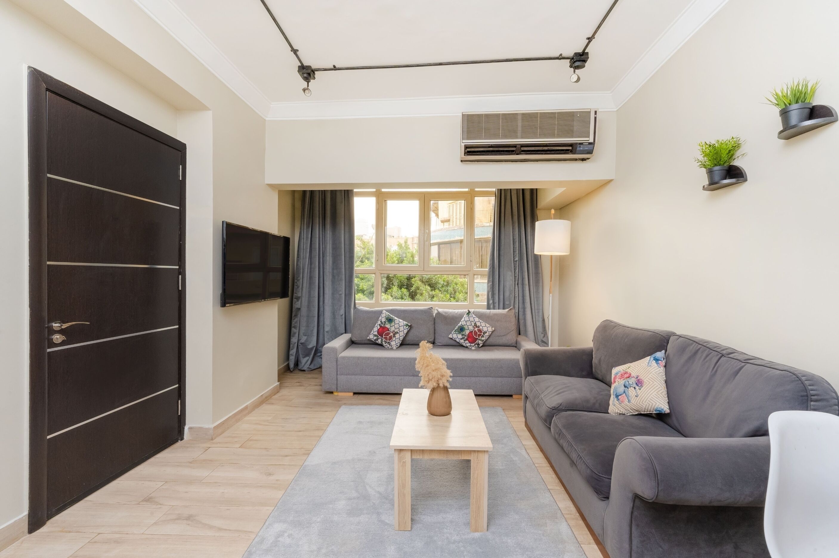 Ein modernes Wohnzimmer mit einer Couch, einem Couchtisch, einem Fernseher und einem großen Fenster mit Vorhängen.