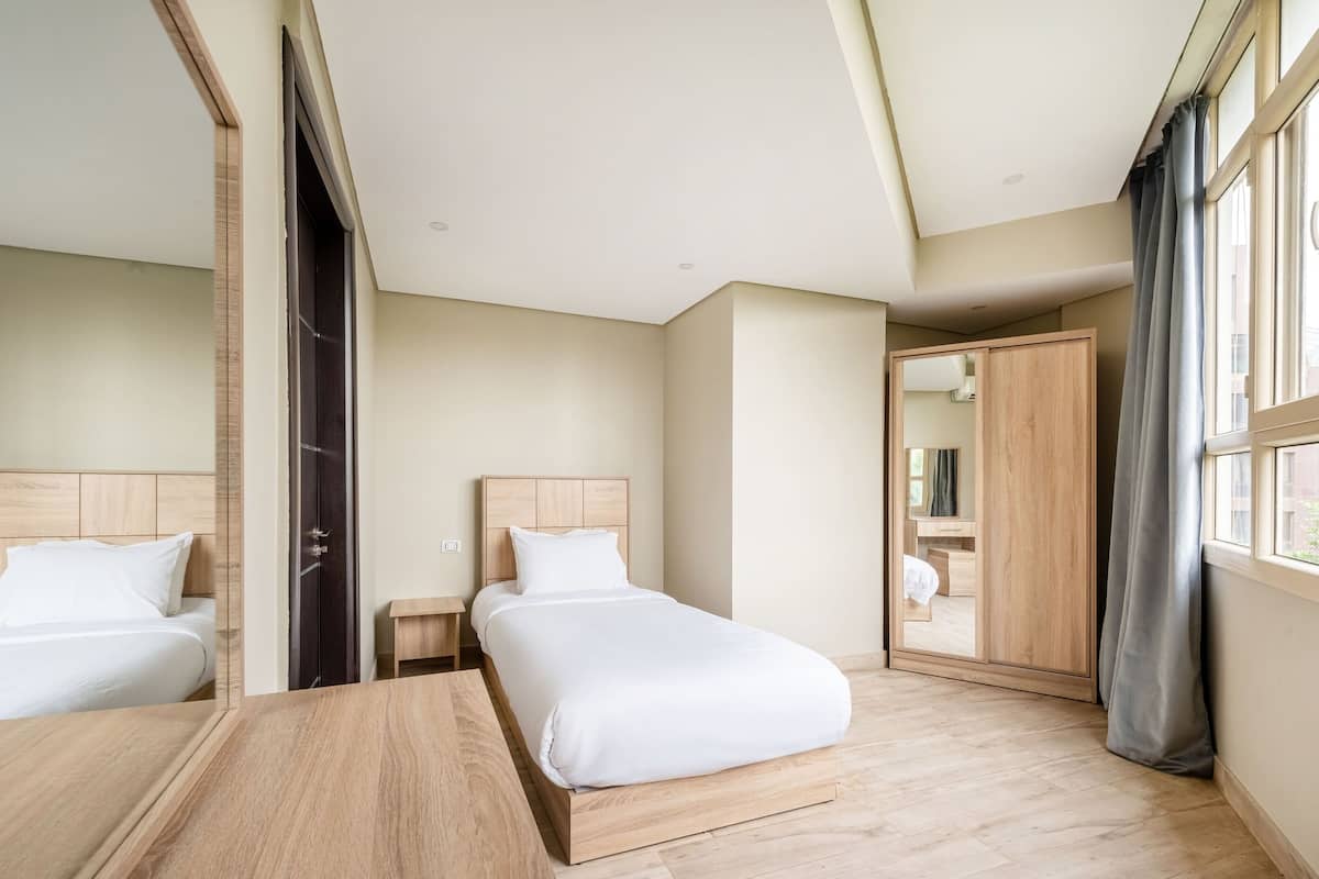 Habitación de hotel con cama, mesitas de noche, un escritorio de madera, armario y una ventana grande con cortinas.