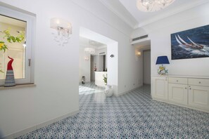 A hallway with patterned floor tiles, a white wall with a painting of a boat, and a white cabinet with a blue lamp. - Villa Costa Incantata with Jacuzzi and Stunning Amalfi Sea Views (Amalfi)