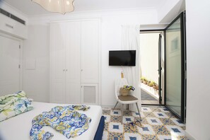 Une chambre d’hôtel avec un lit, une télévision, une chaise avec un panier, et un balcon agrémenté de plantes en pot.