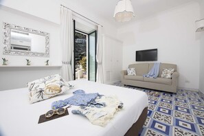 A bedroom with a bed, a sofa, a TV, a mirror, and a bathroom with a shower. - Villa Costa Incantata with Jacuzzi and Stunning Amalfi Sea Views (Amalfi)