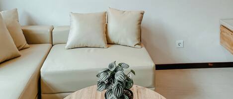 En stue med en beige sofa, to puder, et rundt træbord med en potteplante og to abstrakte malerier på væggen.