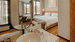 Ein modernes Hotelzimmer mit einem großen Bett, einer Sitzecke, einem Badezimmer mit großem Spiegel und Blick ins Freie.