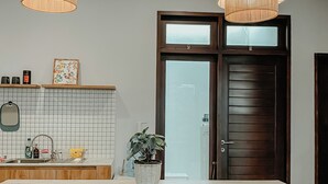 Eine moderne Küche mit einer zentralen Kochinsel, zwei Pendelleuchten, einem Topf mit Pflanze und einer Holztür.