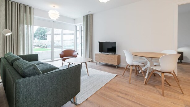 A modern living room with a sofa, a dining table with chairs, a TV, and a large window with curtains. - The Lookout by Dublin At Home (Dublin)