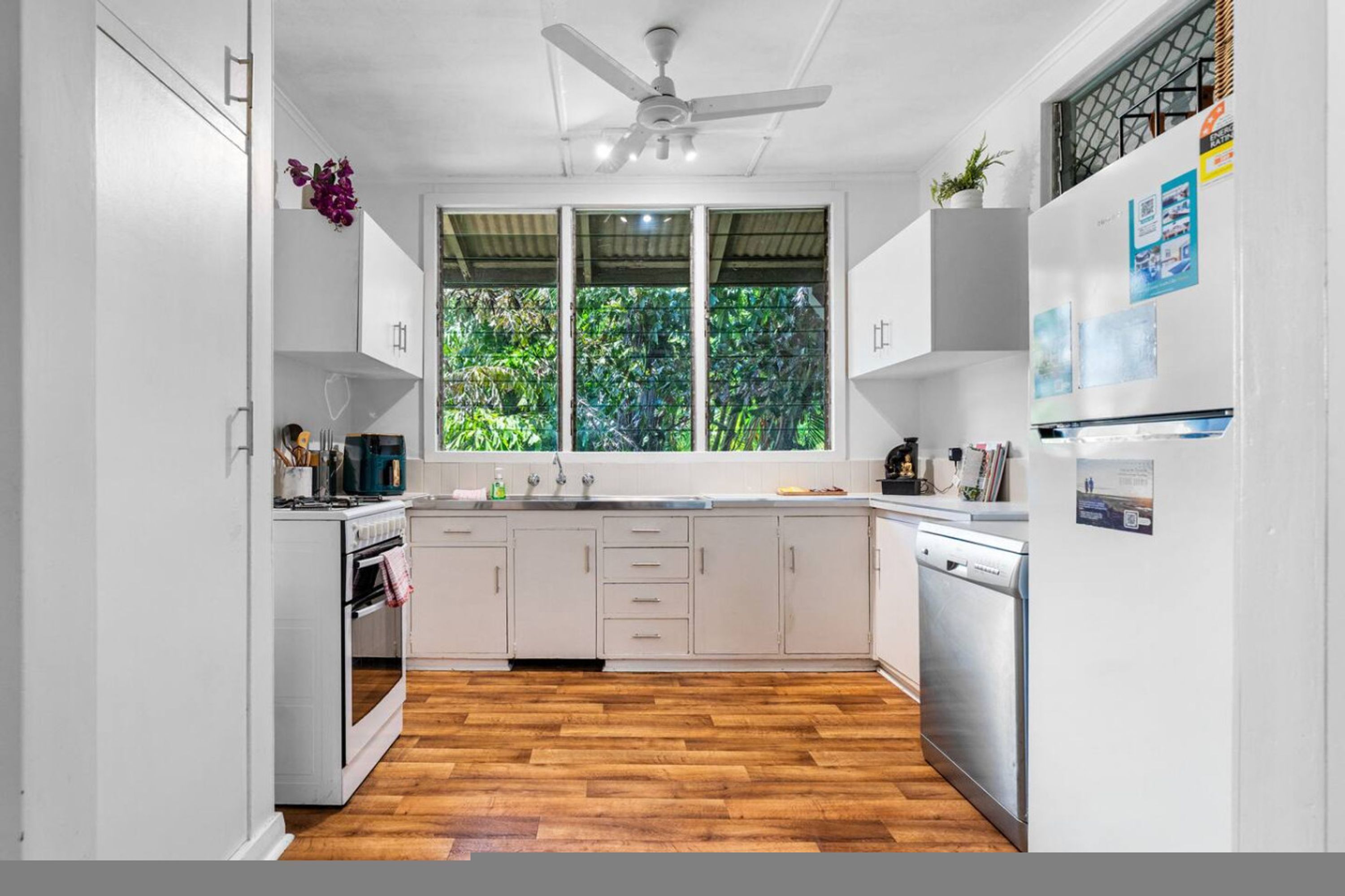 Una cocina moderna con armarios blancos, suelo de madera y un ventanal con vistas a zonas verdes.