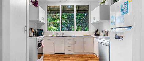 Una cocina moderna con armarios blancos, suelo de madera y un ventanal con vistas a zonas verdes.