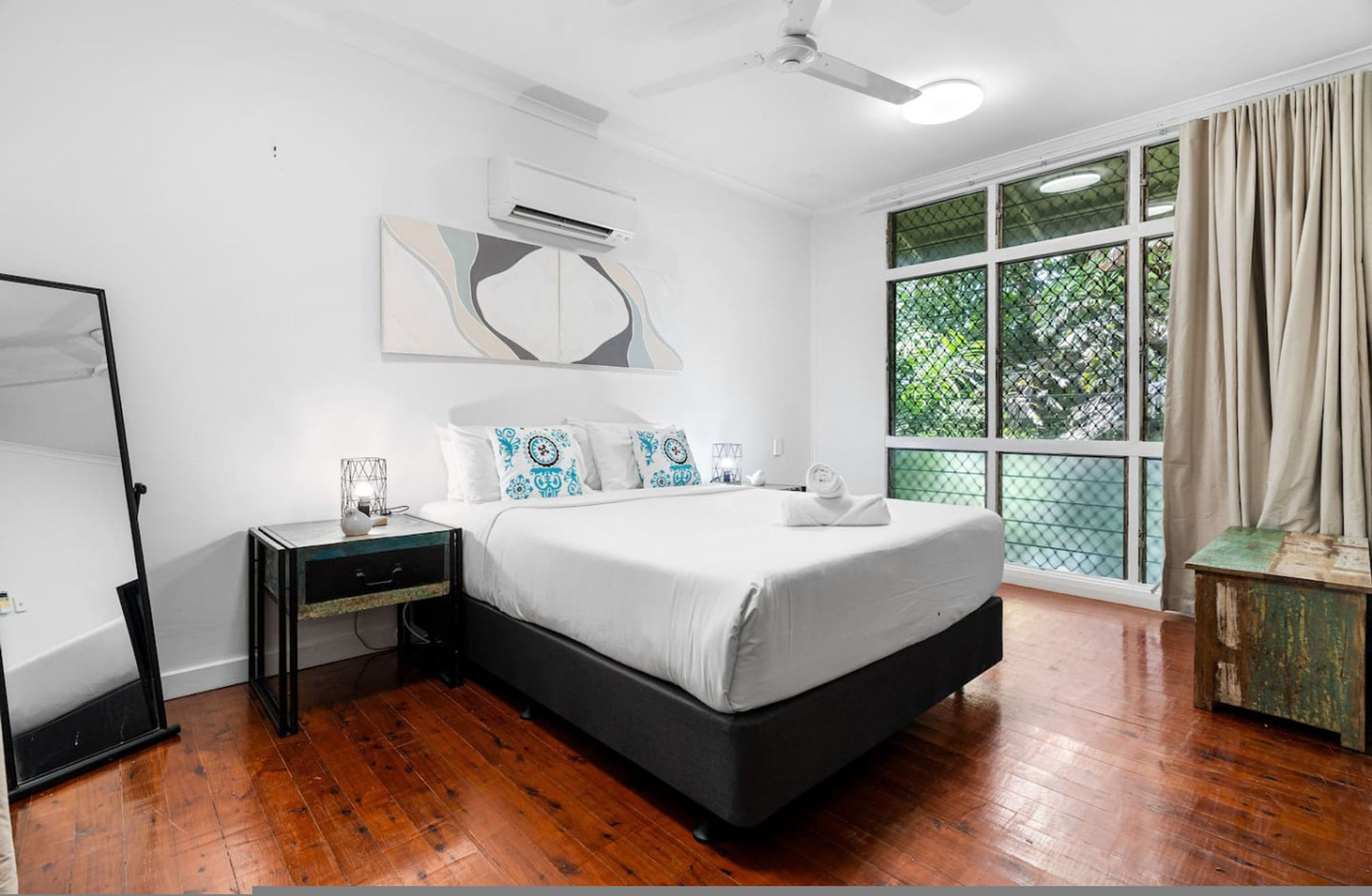 A bedroom with a bed, bedside table, and a large window with curtains.