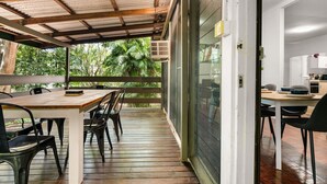 An indoor dining area with a wooden table and chairs, a glass partition, and a view of lush greenery outside. - Zen City Tropics Fenced Yard - Balcony - Desk (Darwin)