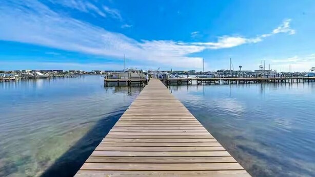 Eine hölzerne Anlegestelle, die sich ins ruhige Wasser erstreckt, mit blauem Himmel darüber.