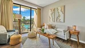 Ein modernes Wohnzimmer mit Sofa, Sessel, Couchtisch und Blick auf Pool und Außenbereich.