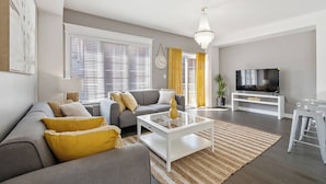 Ein modernes Wohnzimmer mit grauem Sofa, einem weißen Couchtisch, einem Fernseher auf einem weißen Schrank und einer Kristallleuchtre.