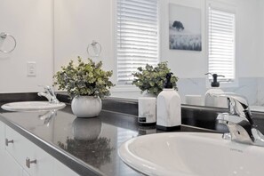 A modern bathroom with a black countertop, two sinks, a large mirror, and decorative plants. - Modern House Steps From Dining, Shopping & Lakes (Aurora)