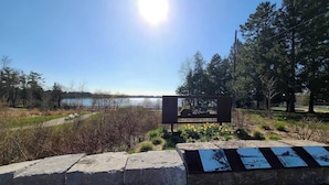 Eine Steinsitzbank mit einer Metallplakette in einem Park mit Blick auf ein See.