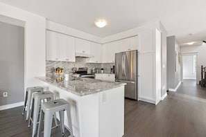 A modern kitchen with white cabinets, a granite countertop, stainless steel appliances, and a central island with bar stools.
