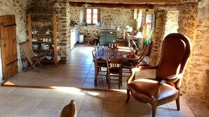 Un comedor rústico con una mesa y sillas de madera, paredes de piedra y una cocina al fondo.