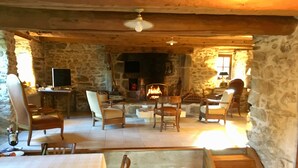 Una sala de estar rústica con suelo de piedra, chimenea, muebles de madera y televisión.