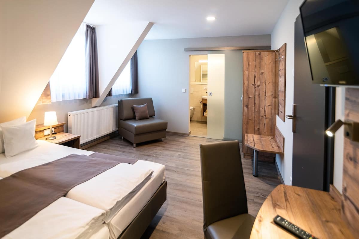 Habitación de hotel moderna con cama, sofá, televisión y una silla de madera.