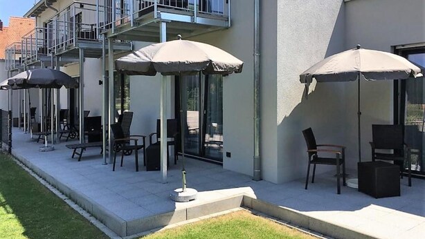 A modern building with outdoor seating areas, including tables and chairs under umbrellas, and a balcony with railings. - Hotel-Gasthof Neue Post (Leutershausen)