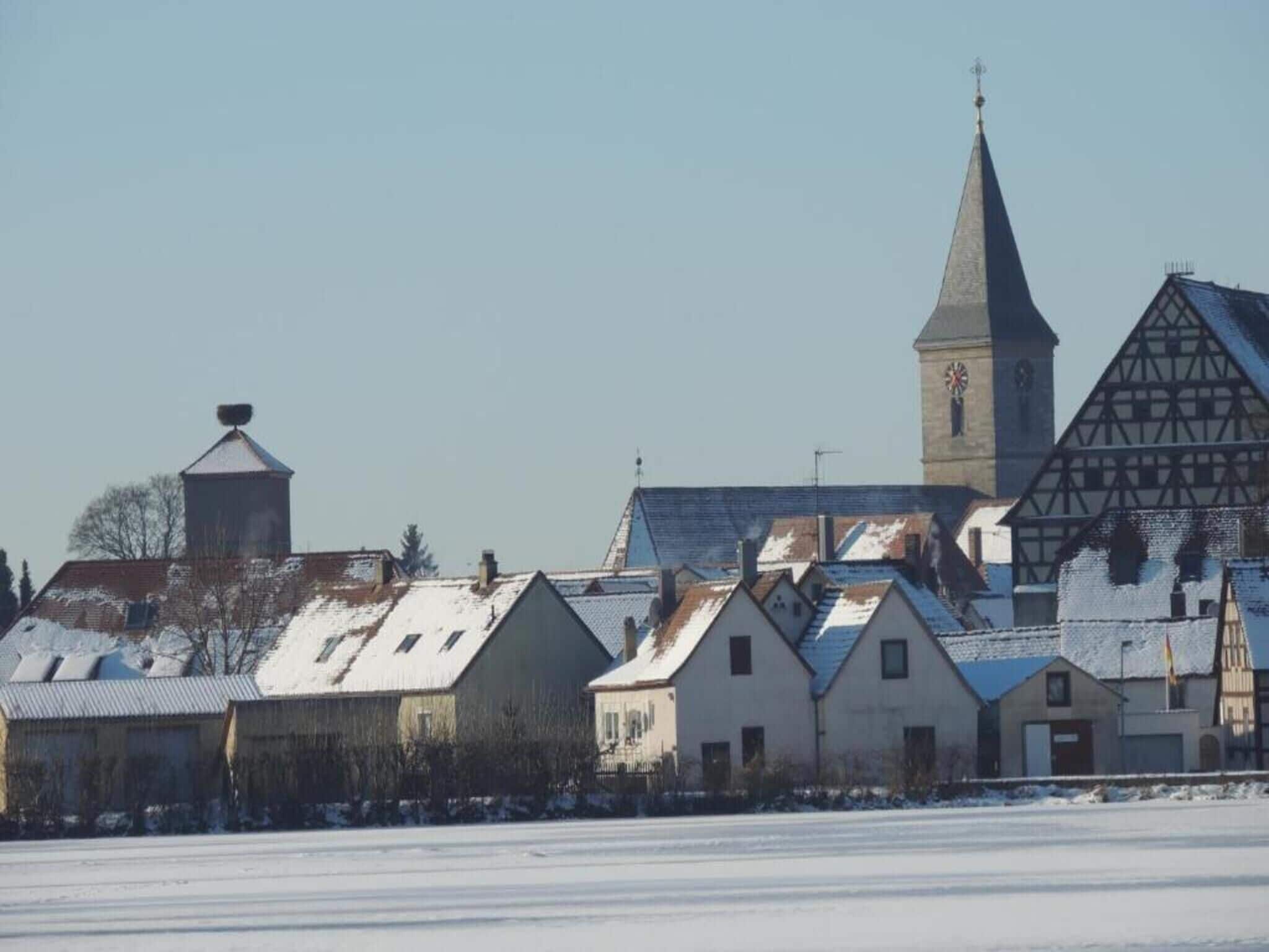 A snow-covered village with traditional half-timbered houses and a church with a tall spire.