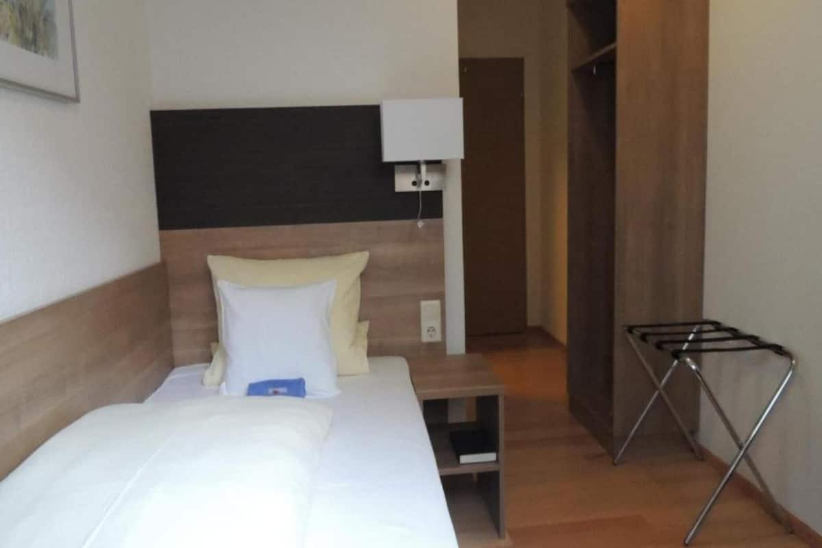 Habitación de hotel con cama, mesita de noche, lámpara, armario y un tendedero.