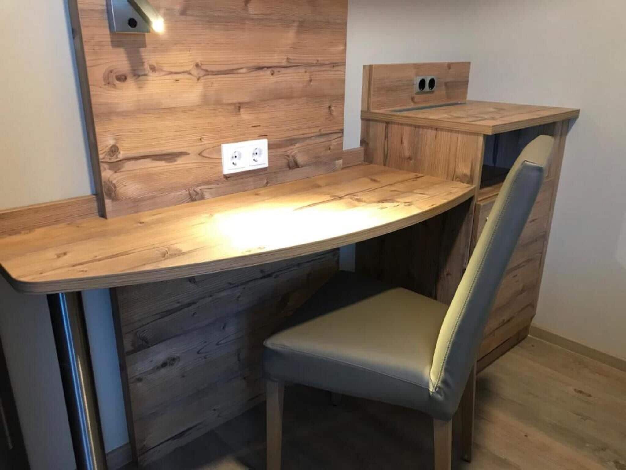 Una habitación compacta y moderna con un revestimiento de madera, un escritorio empotrado y una silla acolchada.