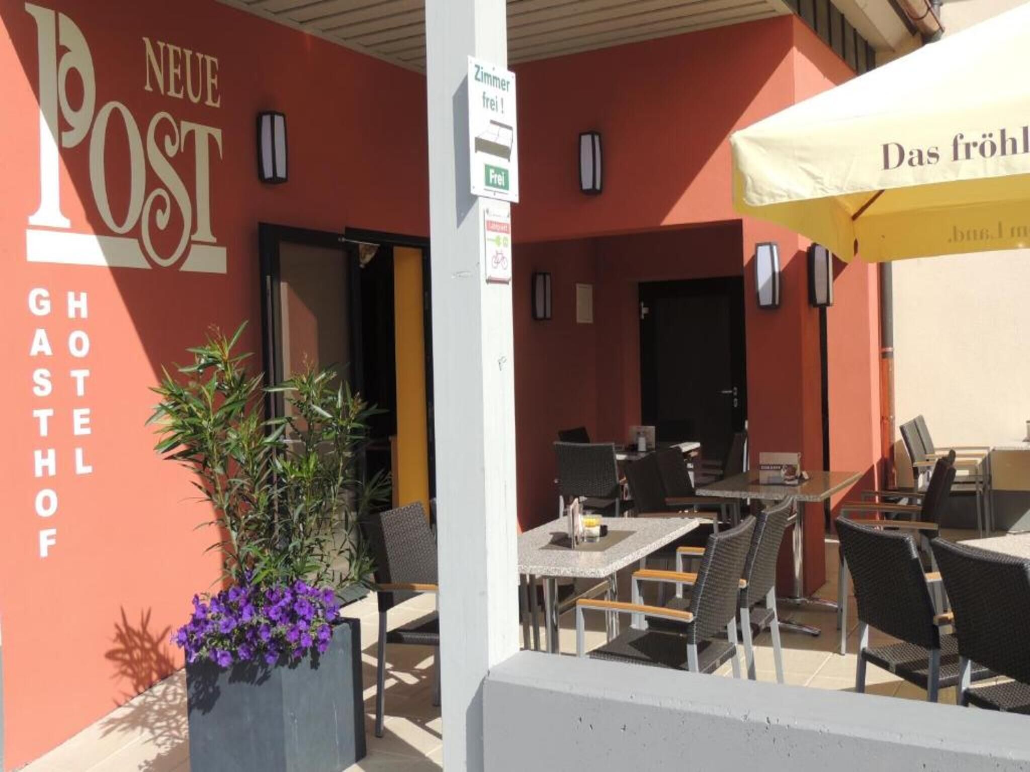 An outdoor seating area with tables and chairs, a sign for 'NEUE POST GHOSTHOFF', and a 'Zimmer frei!' sign indicating available rooms.