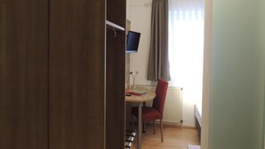 A room with a wooden wardrobe, a desk with a chair, a radiator, and a window with curtains. - Hotel-Gasthof Neue Post (Leutershausen)