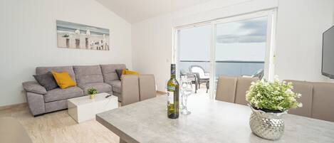 A modern living room with a grey sofa, a coffee table, and a dining table with a bottle of wine and a glass.