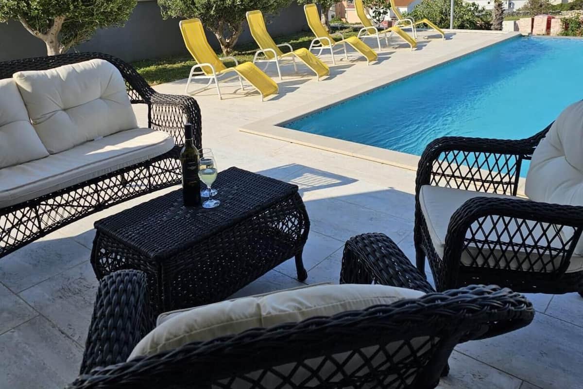 Un área junto a la piscina con sillones de descanso, un sofá y una mesa con una botella y una copa.