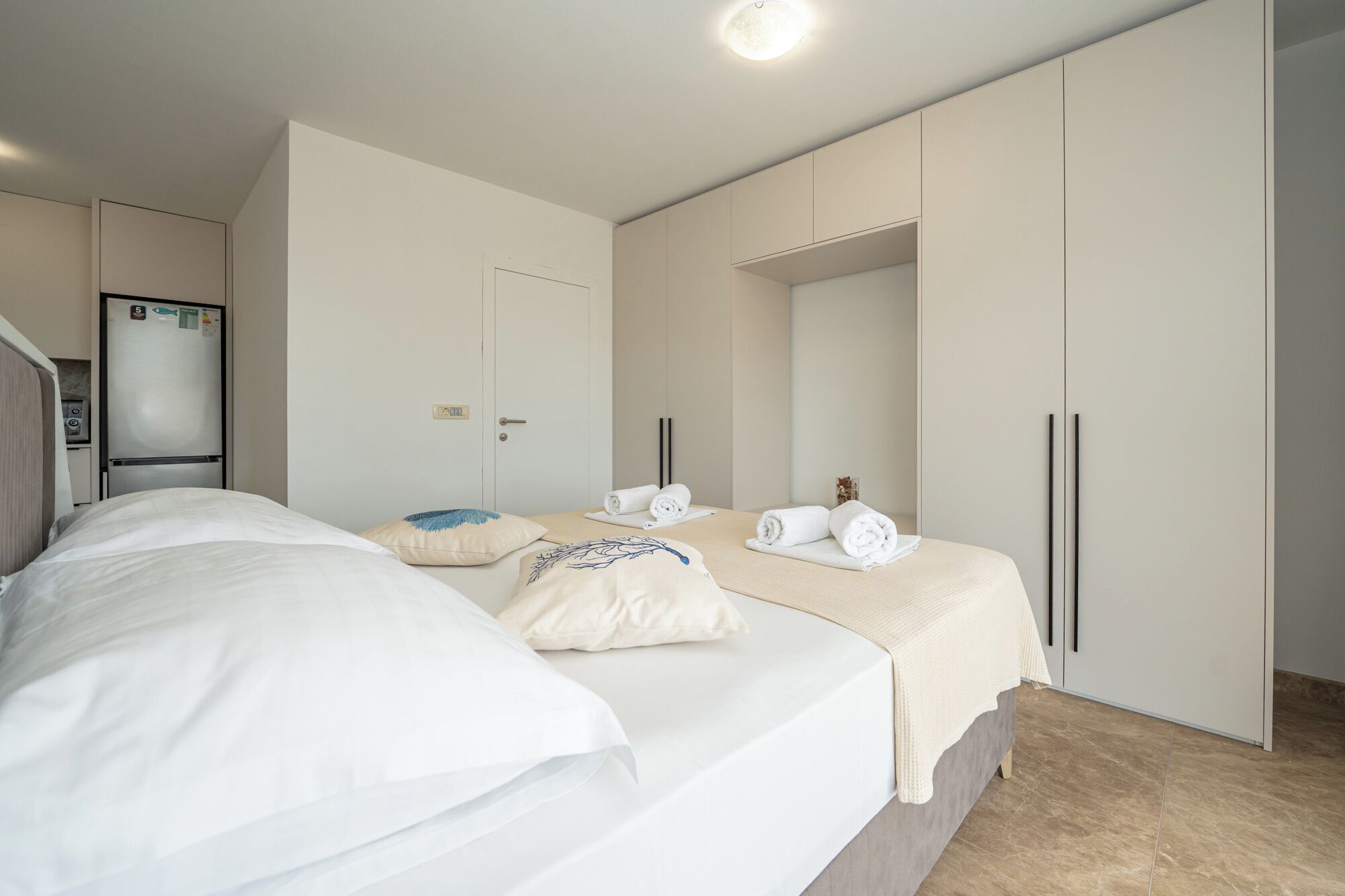 A hotel room with a bed, a wardrobe, a mirror, and a refrigerator.