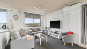 Uma sala de estar moderna com televisão de tela plana, sofás cinzas, uma mesa de centro e uma grande janela com vista.